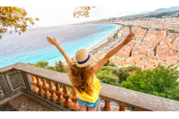 Photo d'une femme les bras écarté, située sur la colline du chateau à Nice, avec la ville en fond